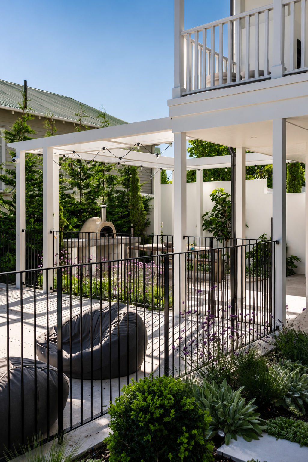 Luxury outdoor entertainment area featuring black steel pool fencing, white pergola, outdoor pizza oven, landscaped garden and modern patio in Auckland, New Zealand.