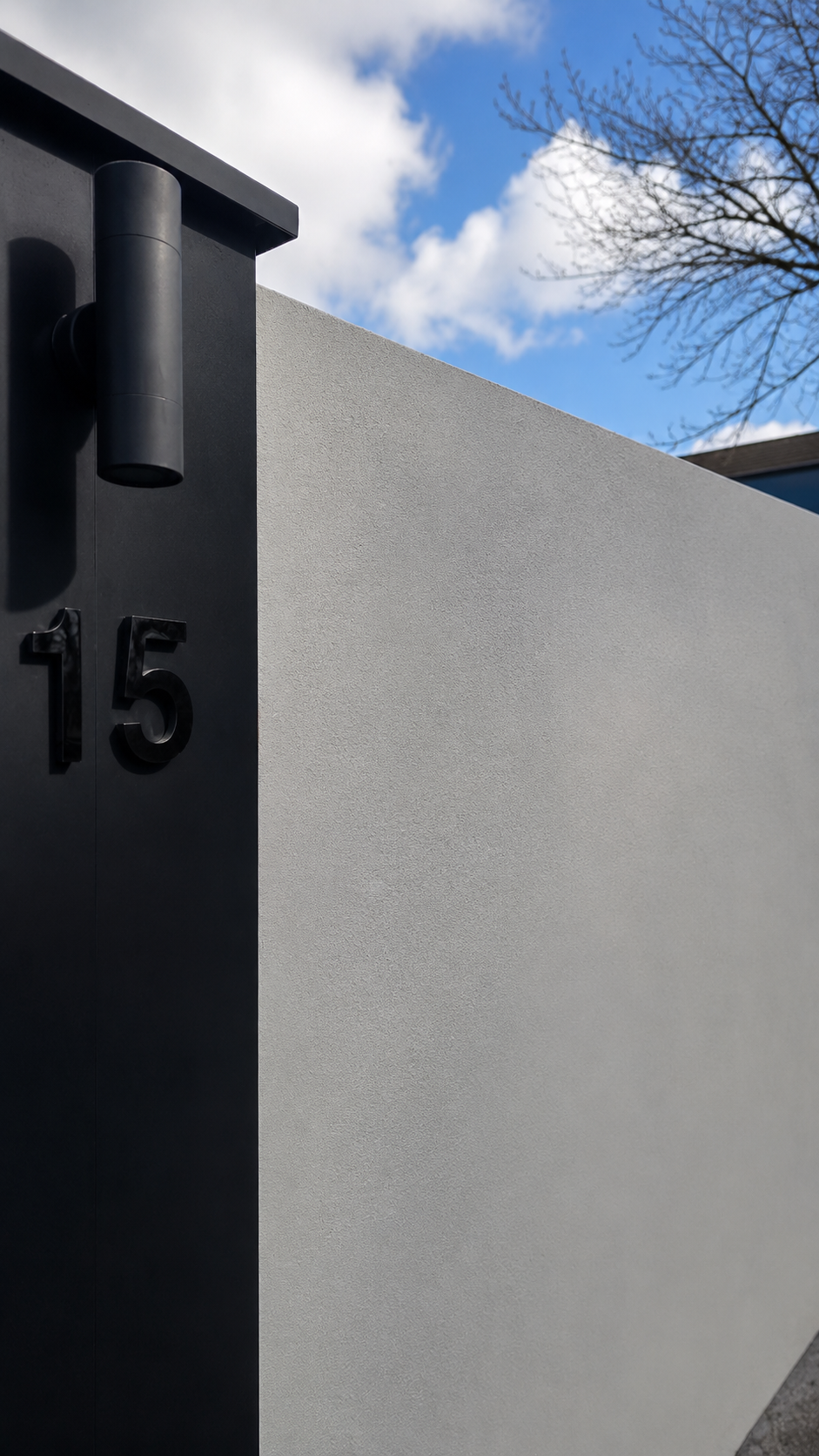 Modern rendered boundary wall with matte black entry pillar, house number 15 and architectural wall light at an Auckland residential property.