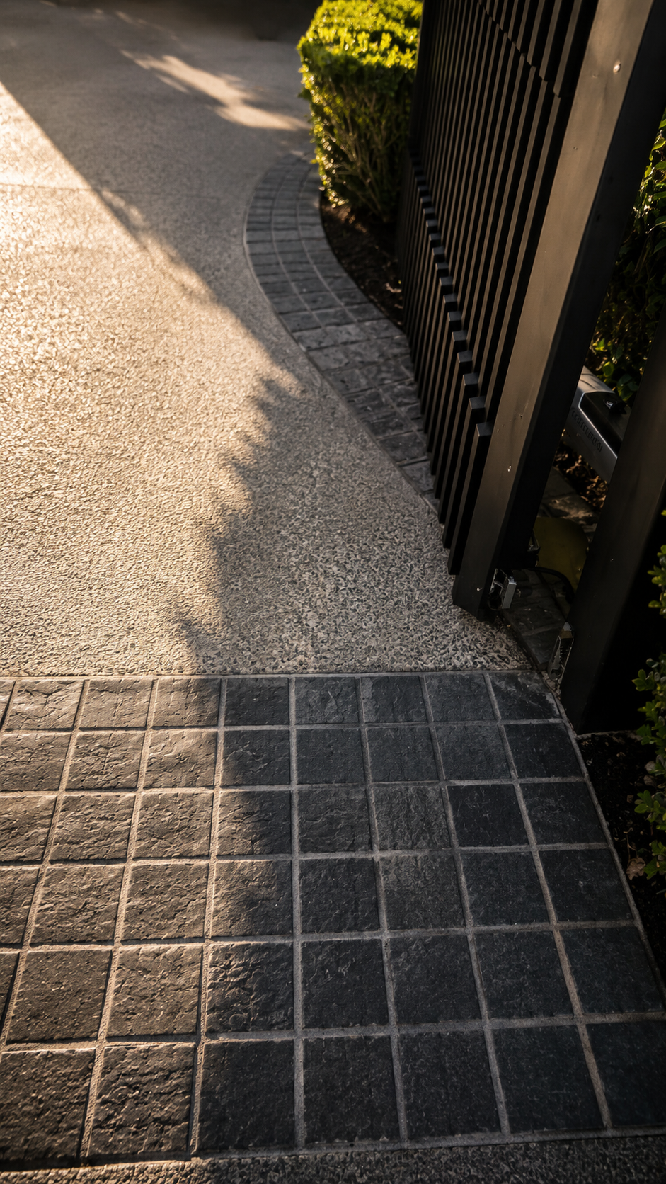 Bluestone cobble border framing an exposed aggregate concrete driveway beside a modern sliding gate entrance.