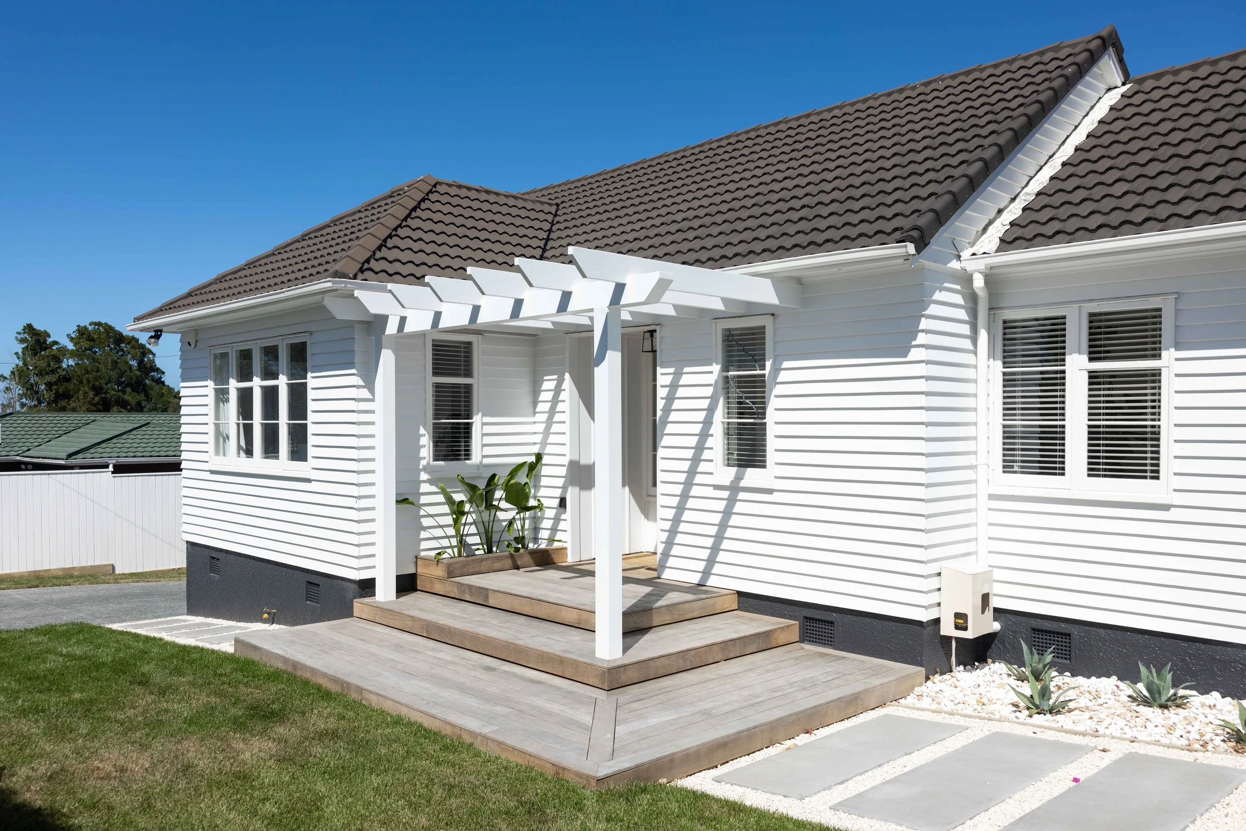 Front entrance featuring a white pergola, timber decking, architectural planting, and modern pathway design creating a welcoming residential entry.