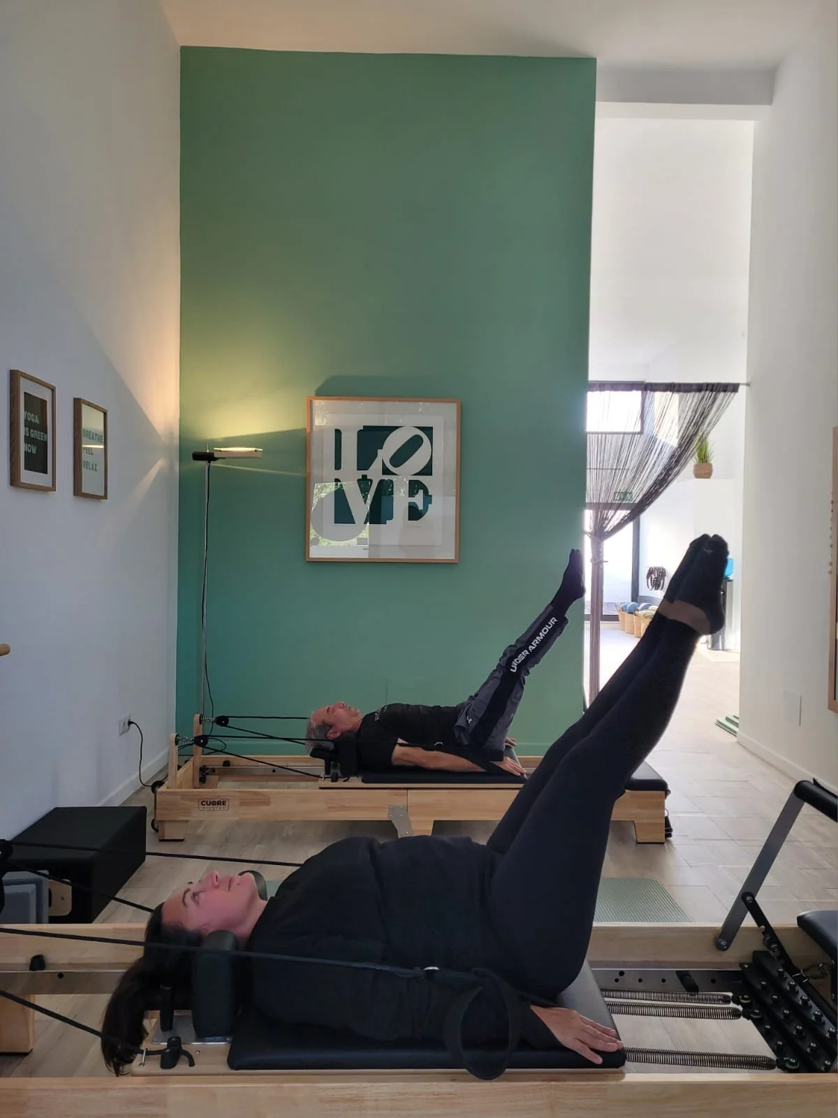 Dos personas haciendo terapia con máquinas de rehabilitación en un espacio interior con decoración moderna y cuadros en las paredes.