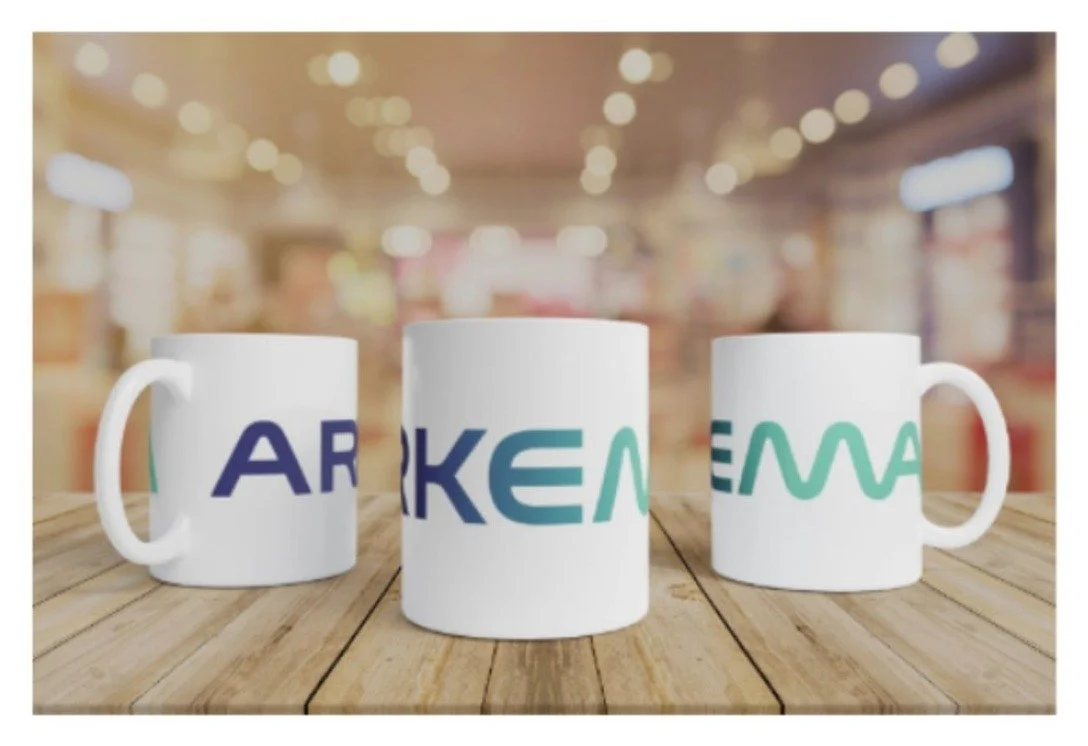 Trois tasses blanches personnalisées avec un logo coloré, posées sur une table en bois dans un café flou.