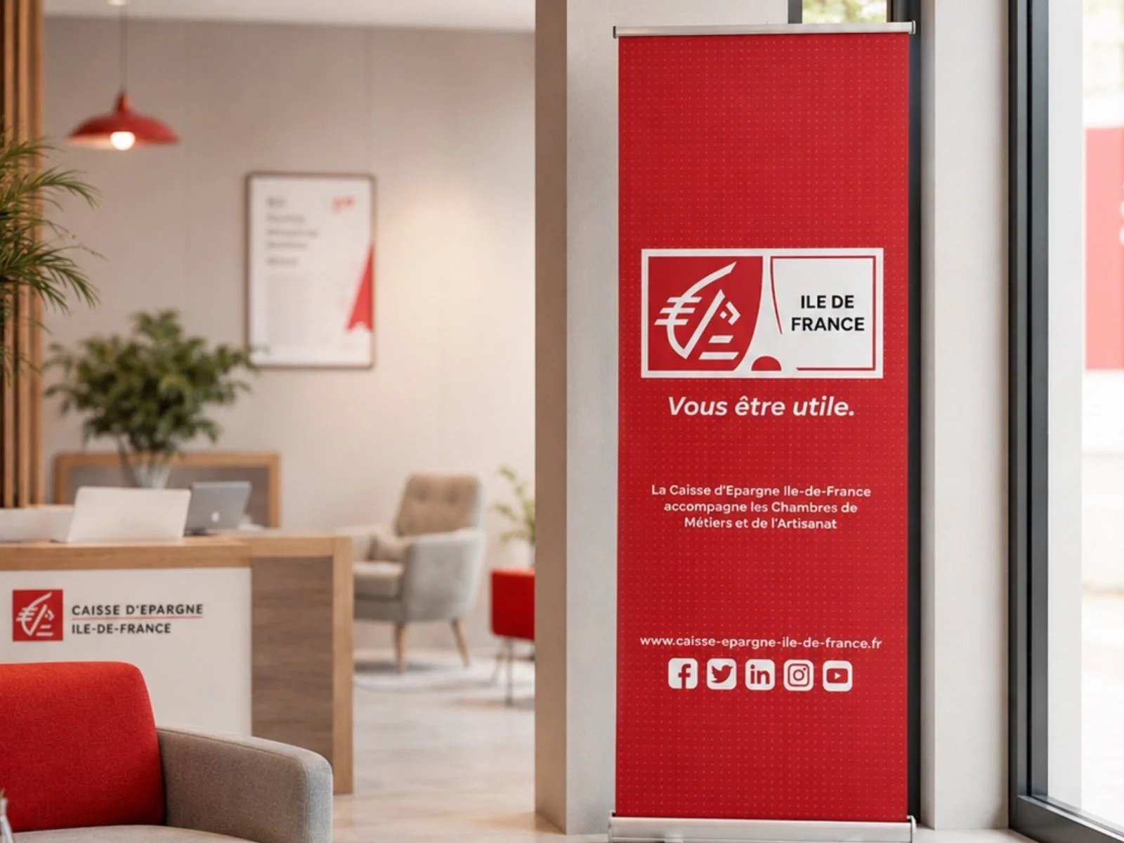 Kakémono rouge de la Caisse d’Épargne Île-de-France dans un espace d’accueil professionnel, avec comptoir et mobilier de bureau.