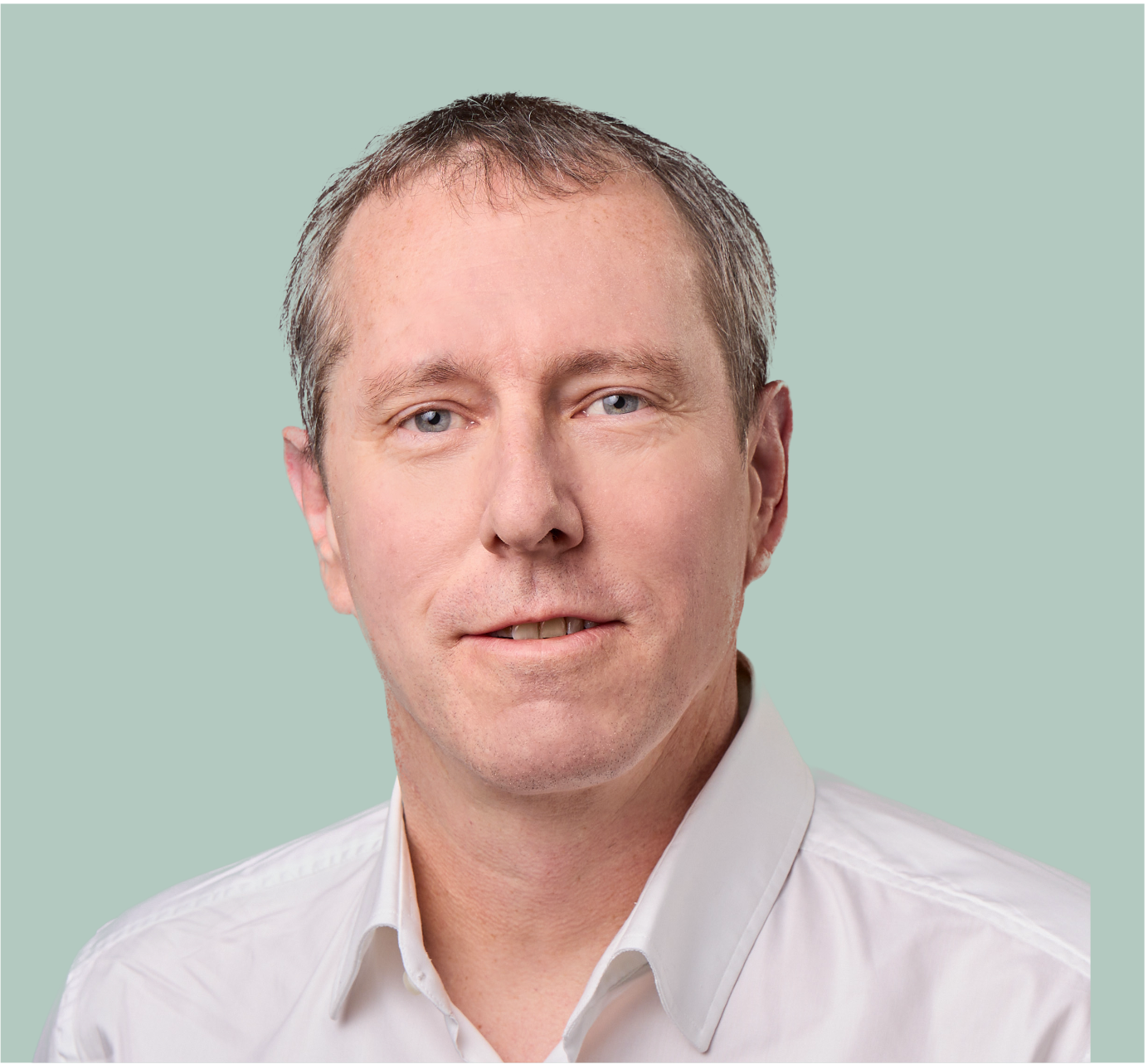 Porträt eines Mannes mit hellblauen Augen, kurzem braunem Haar und weißem Hemd vor einem grünen Hintergrund.
