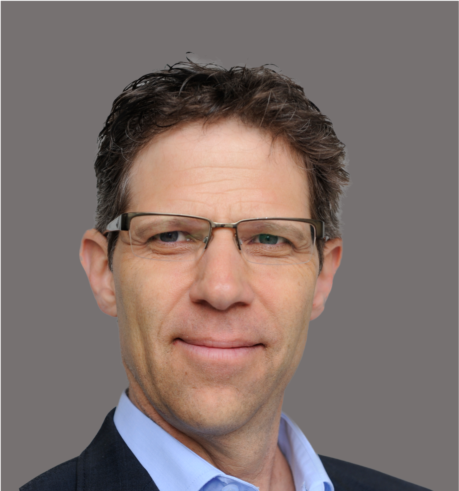 Porträt eines Mannes mit dunklen Haaren, Brille und Anzug vor grauem Hintergrund.