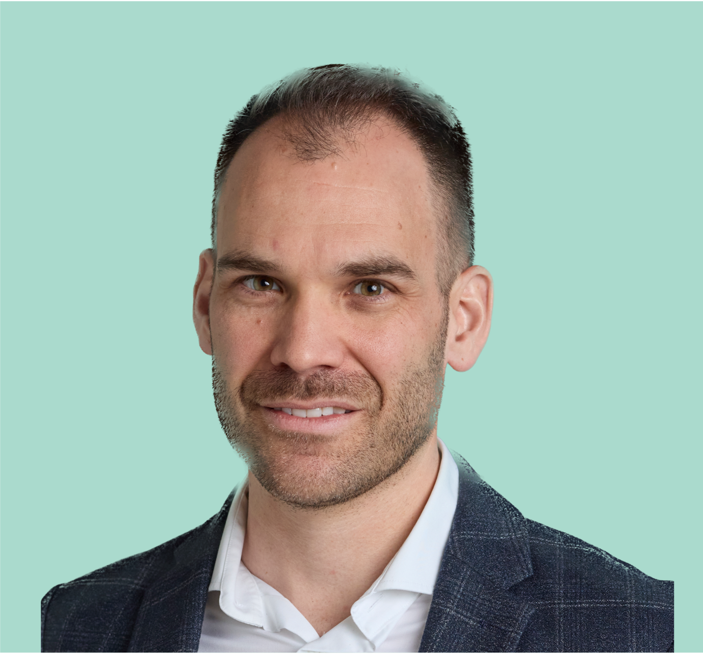 Porträt eines Mannes mit dunklem, kurzem Haar, Bart und Anzug vor hellgrünem Hintergrund.