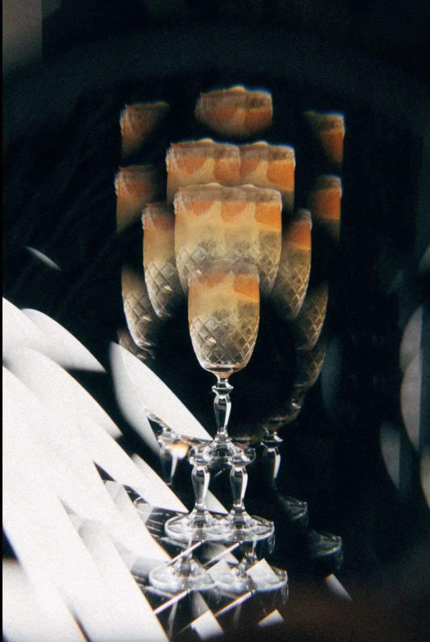 Multiple champagne flutes arranged in a line, with a blurred, repetitive reflection of the same glasses behind them, creating a mirrored effect.