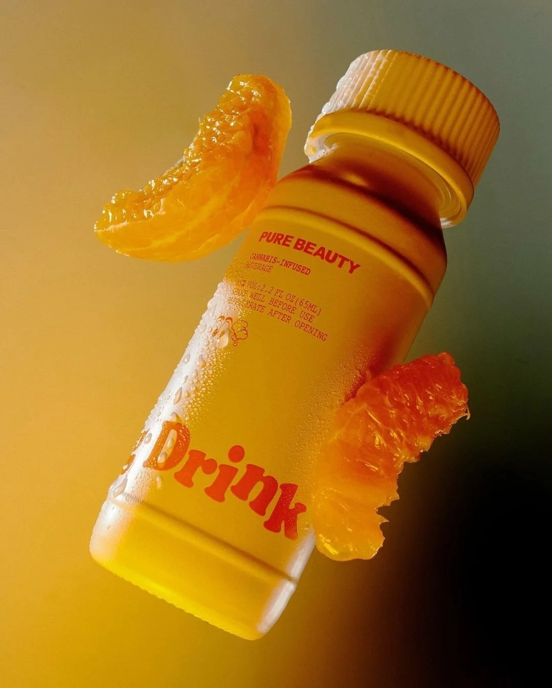 A yellow bottle labeled "Pure Beauty" with orange text that says "Drink" and two orange slices attached to the bottle, one on each side.