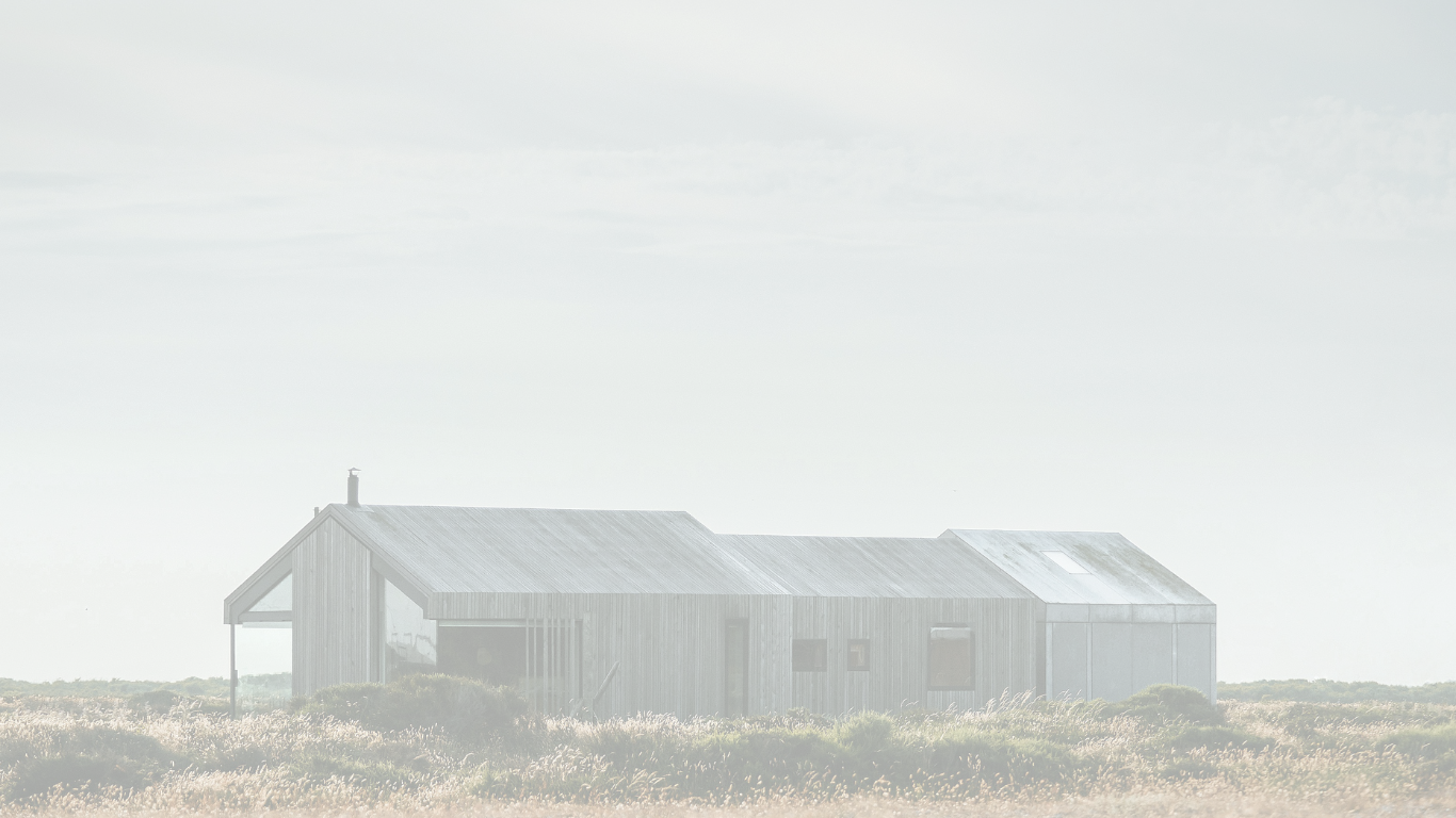 A modern rural house with a metal roof, situated in an open field with tall grass, under a cloudy sky.
