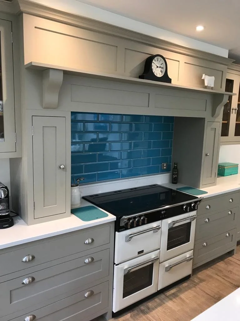 A kitchen with gray cabinetry, a white double oven stove, a blue tile backsplash, and a countertop with small appliances and decorative items.