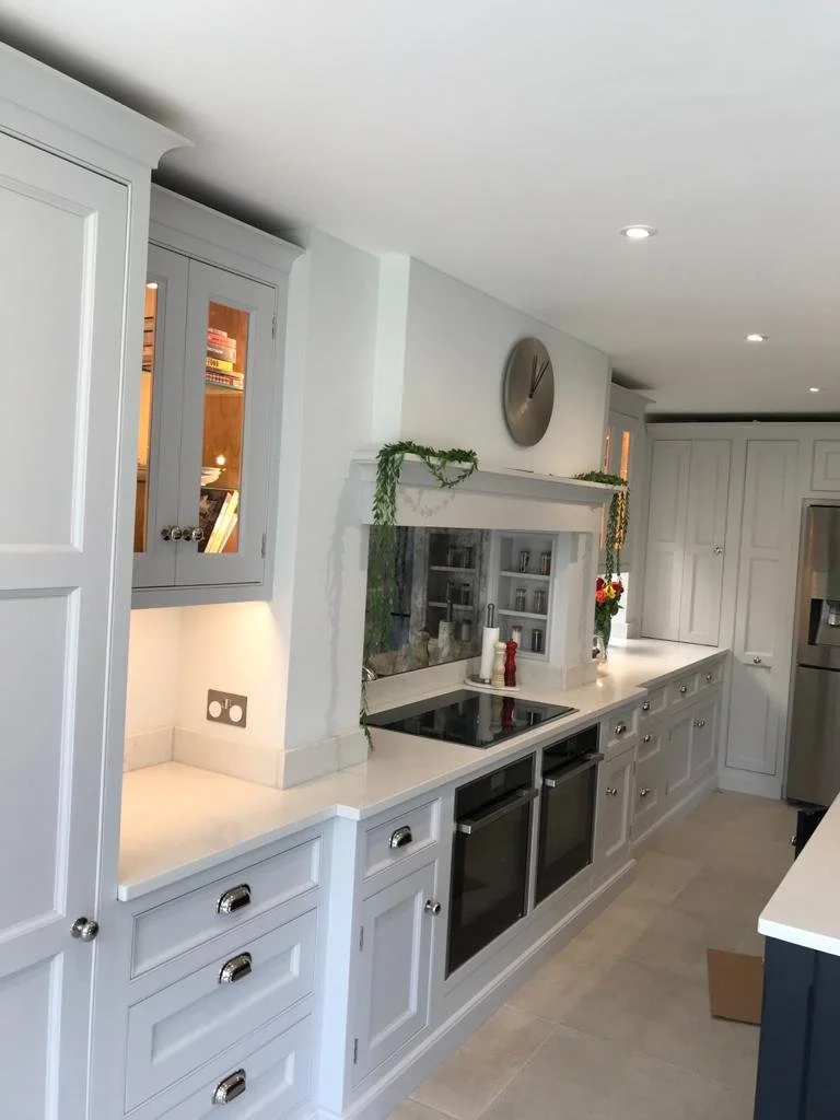 Modern kitchen with white cabinets, black stovetop, and stainless steel refrigerator, decorated with a clock and green garland.