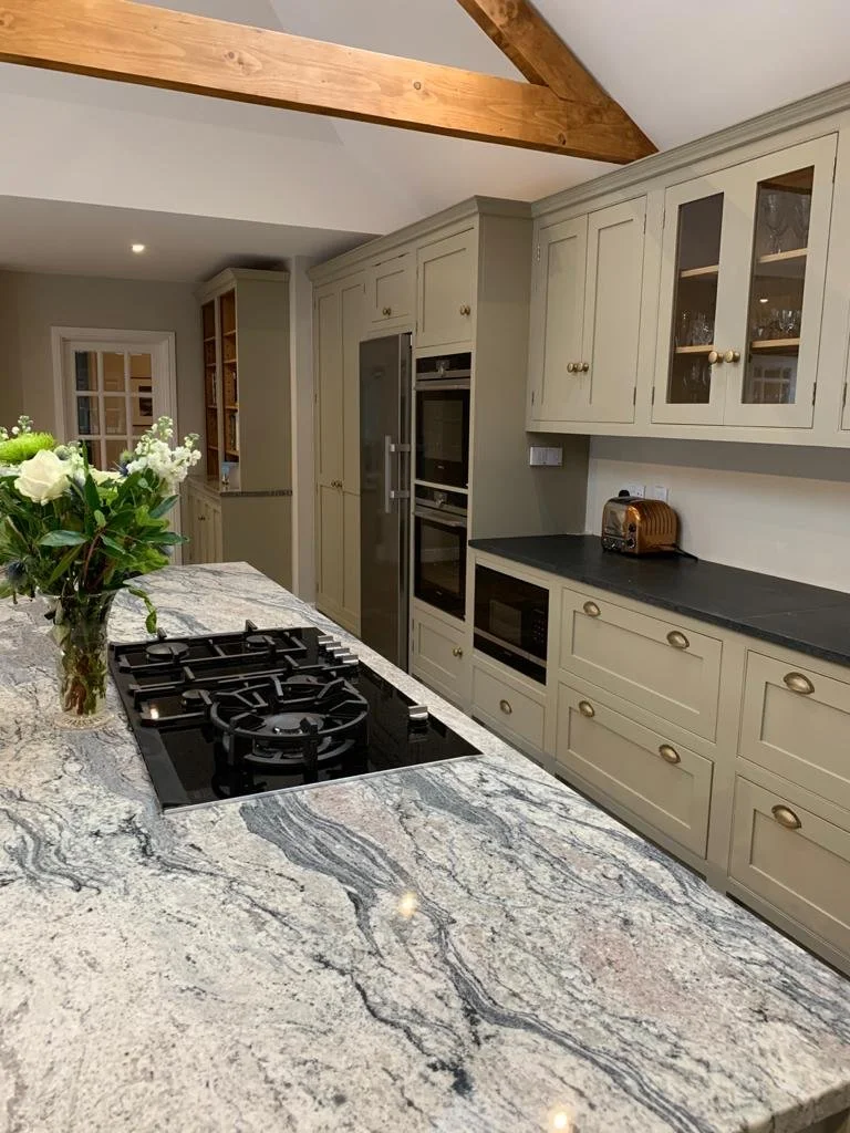 Modern kitchen with granite countertop, light green cabinets, built-in oven and microwave, toaster, and a vase with white flowers.