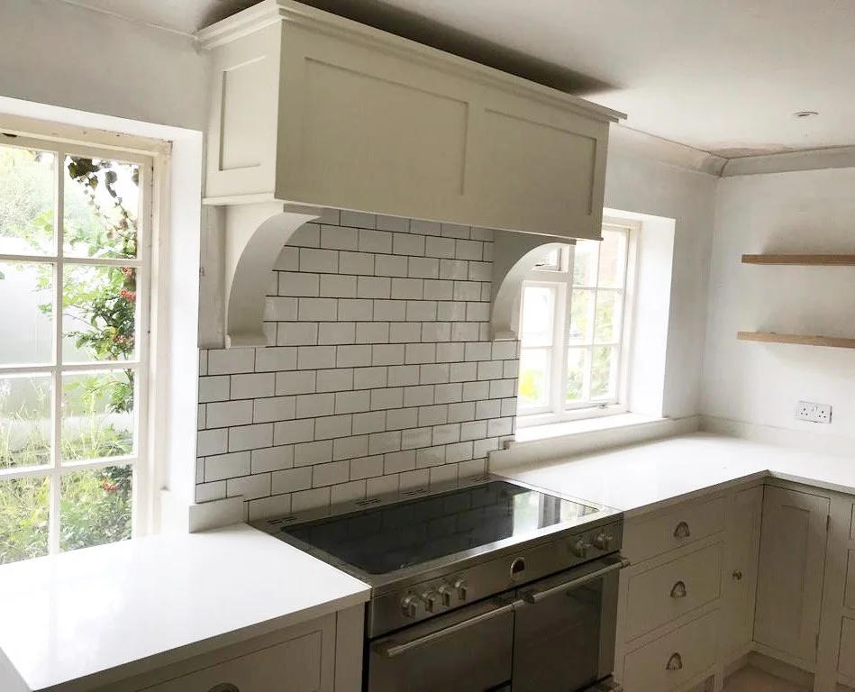 White kitchen with white cabinets, a black electric stove, white subway tile backsplash, and two windows with views of greenery outside.
