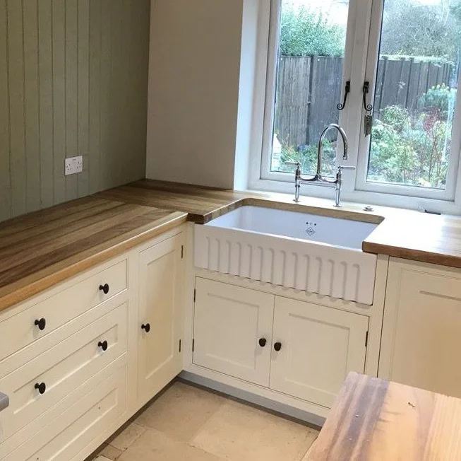 Kitchen with cream cabinets, wooden countertops, farmhouse sink, and window overlooking a garden.