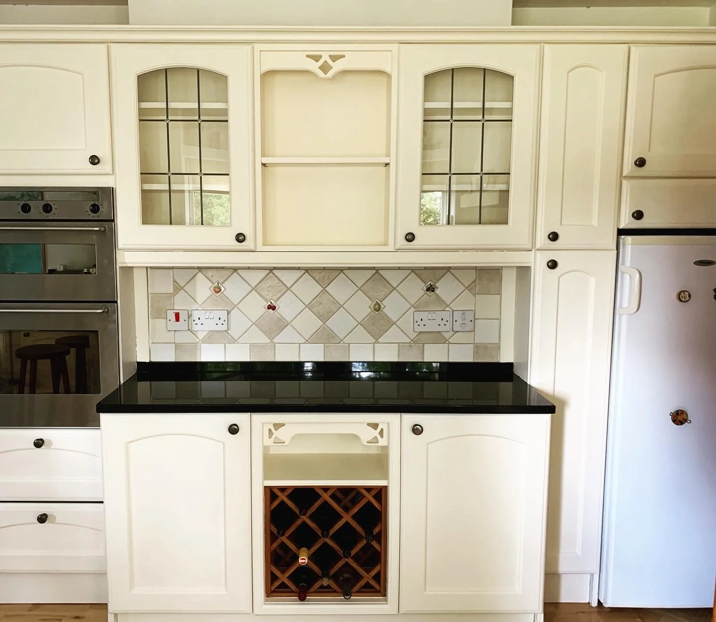 Kitchen with white cabinets, black countertop, tiled backsplash, built-in appliances, and a wine rack.