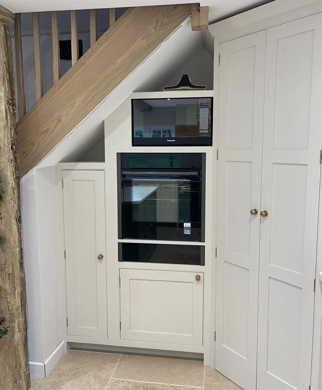 Built-in kitchen under staircase with white cabinets, black microwave, and oven.