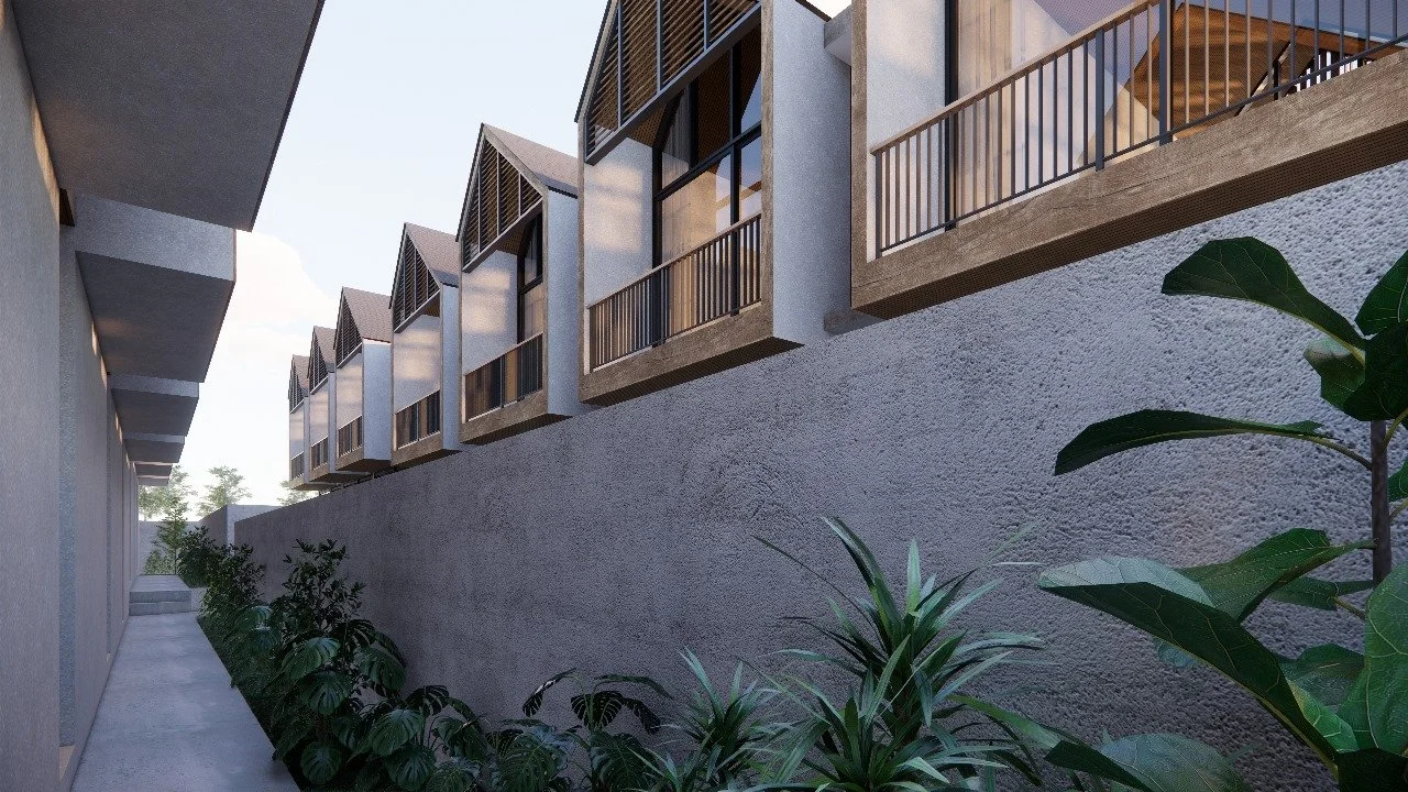 A modern apartment building with multiple balconies and black railings, viewed from a concrete walkway with green plants along the wall.
