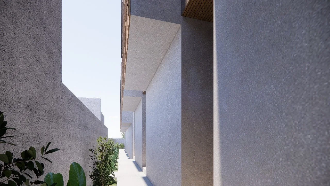 A narrow outdoor corridor between a textured gray wall and a modern building with white walls and wooden accents, with green plants along the walkway under a clear sky.