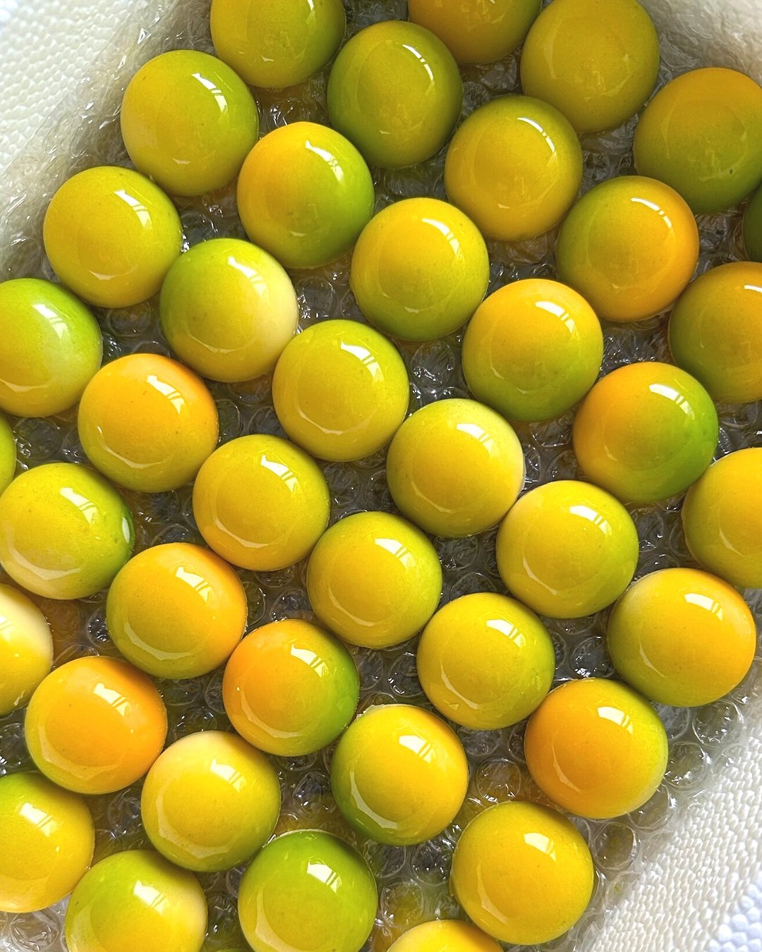 A collection of glossy yellow and green marbles piled on bubble wrap.