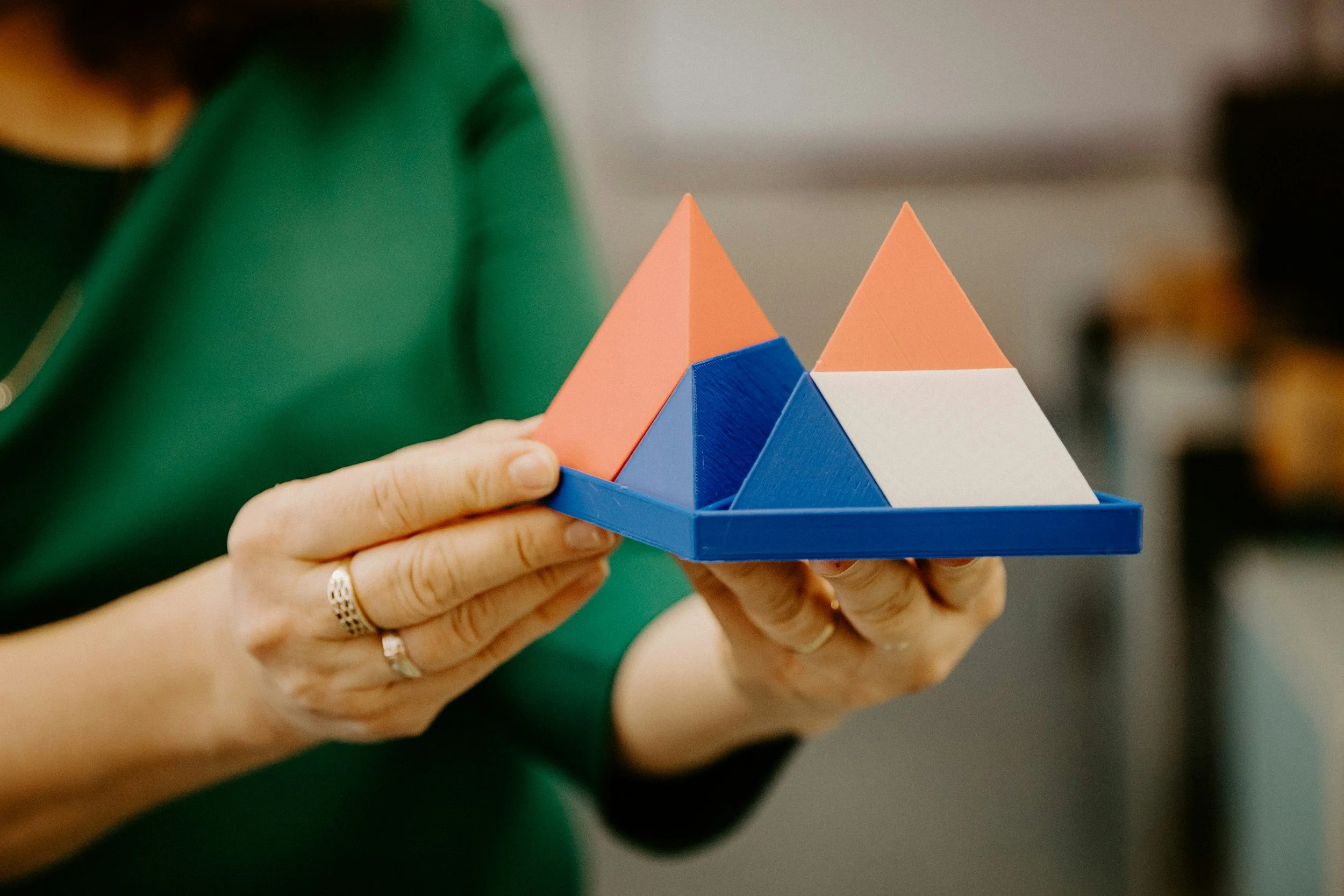 Person holding a colorful geometric puzzle with triangular and square shapes in blue, pink, white, and orange.