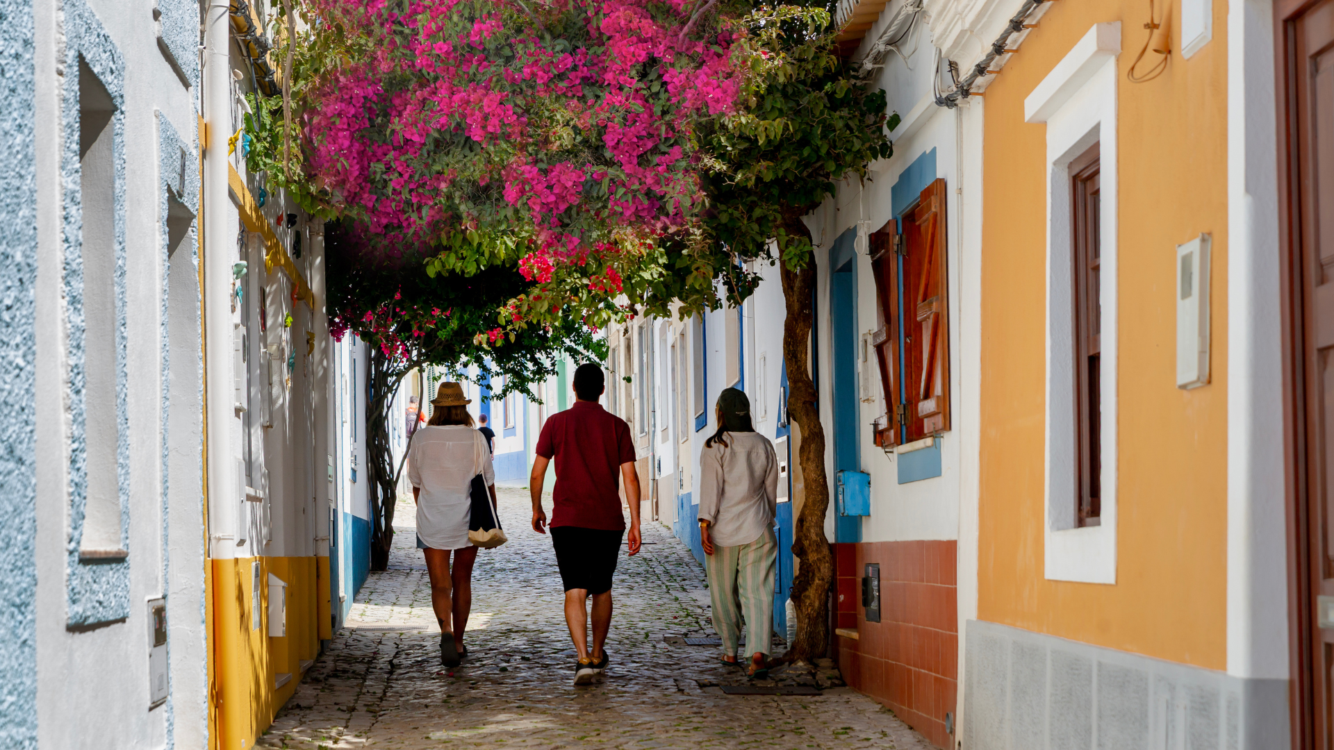 Three people strolling along the flower-filled street in Ferragudo, in the Algarve.