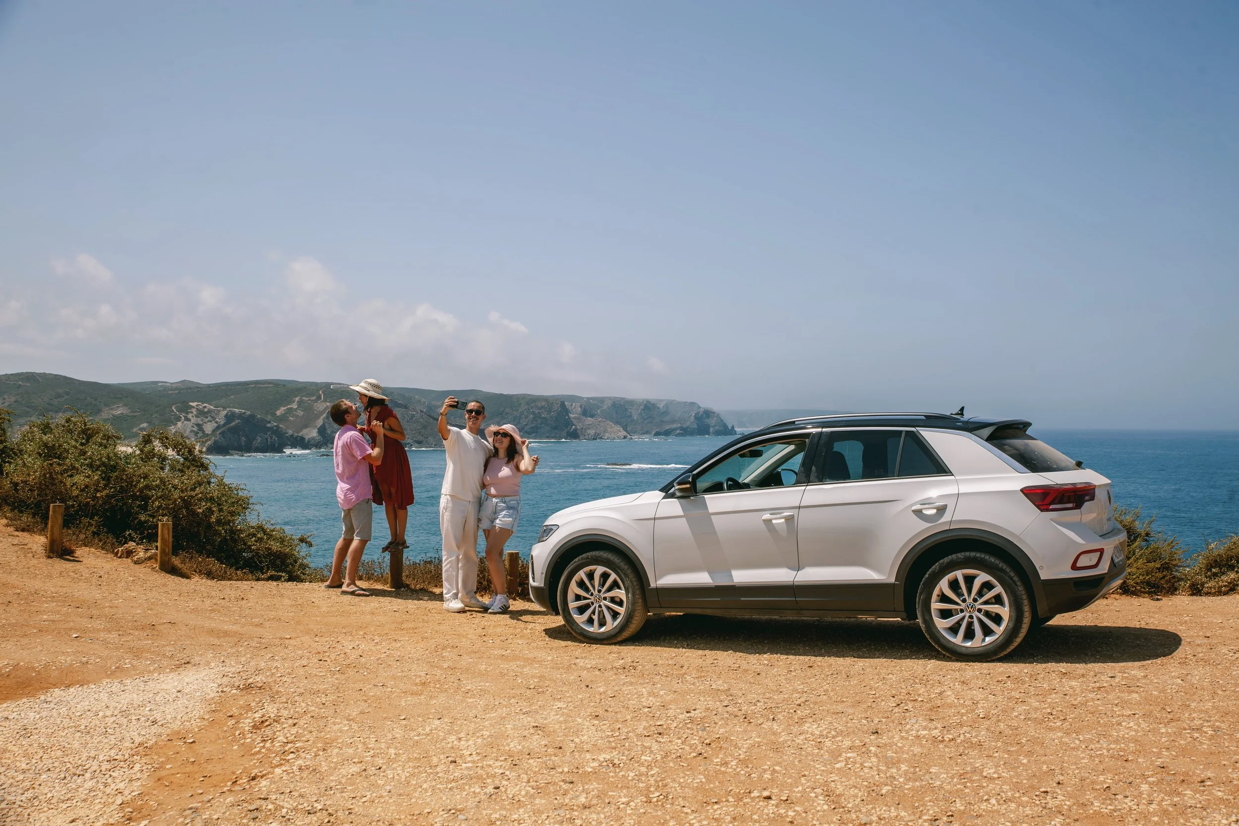 Group of friends by a car with Praia do Amado on background 