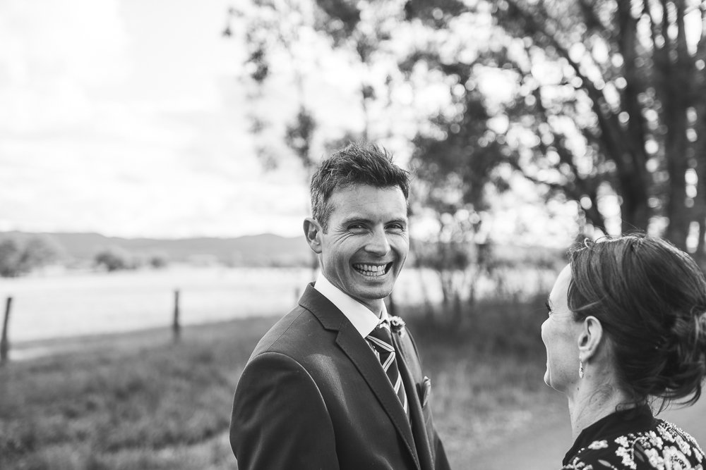 A man in a suit smiling and looking at a woman outdoors with trees and a field in the background in black and white.