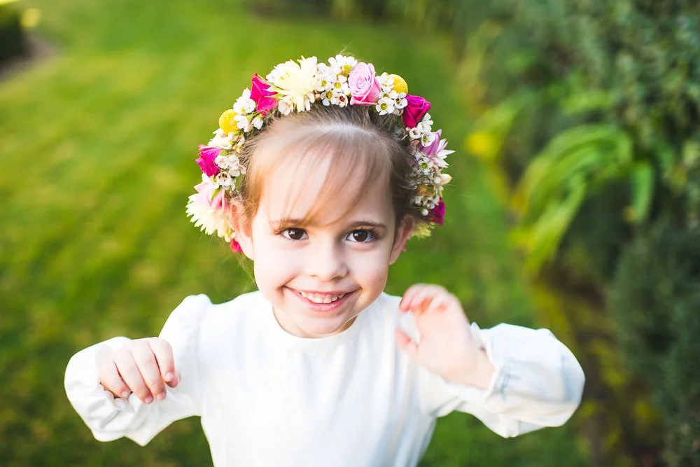 A young girl with a floral crown smiling outdoors.