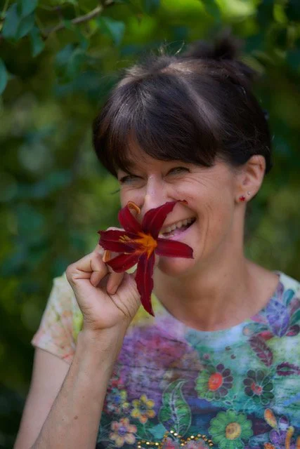 Frau hält eine rote Blume vor das Gesicht und lächelt.