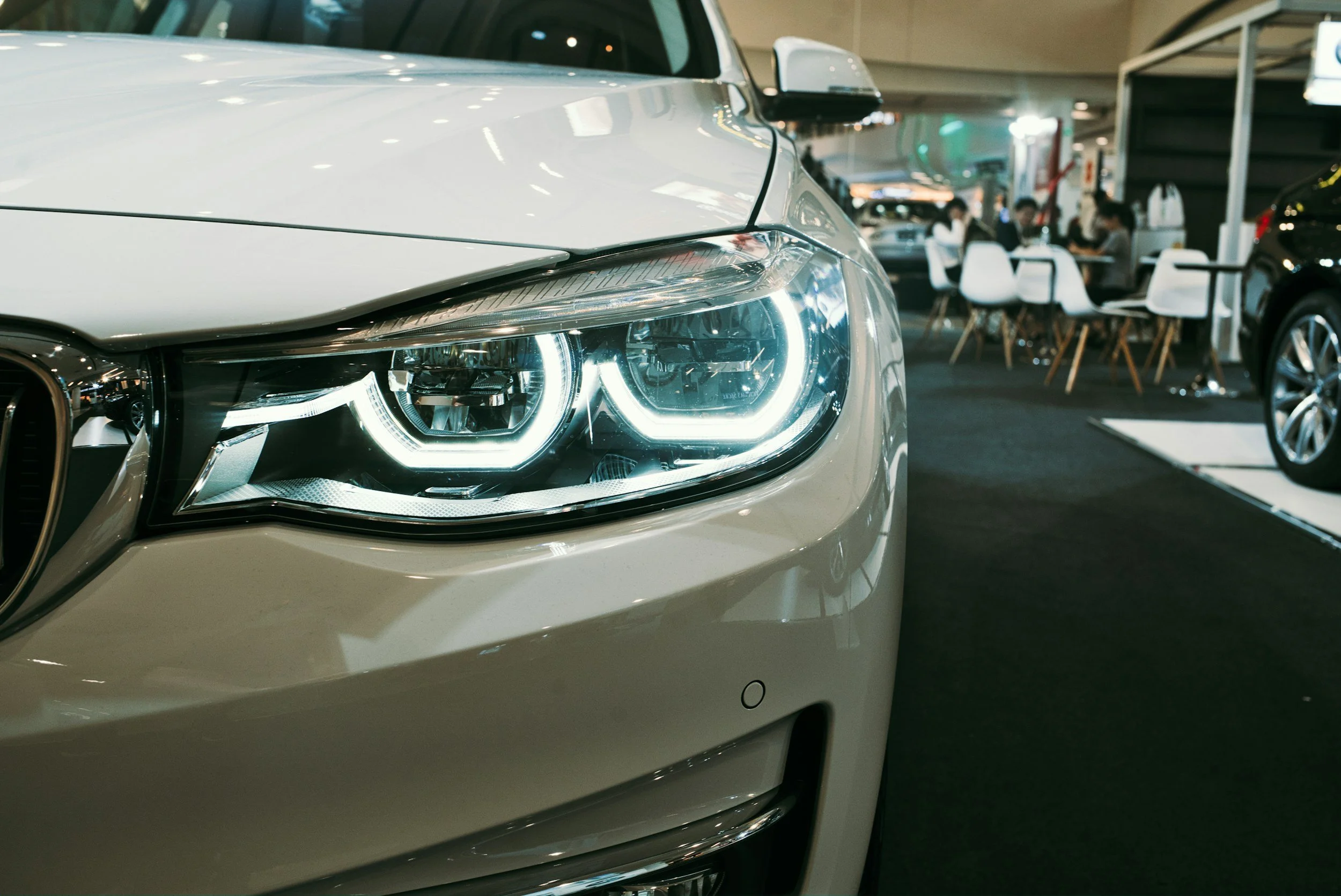Close-up of a white car's front headlight at an indoor car dealership.