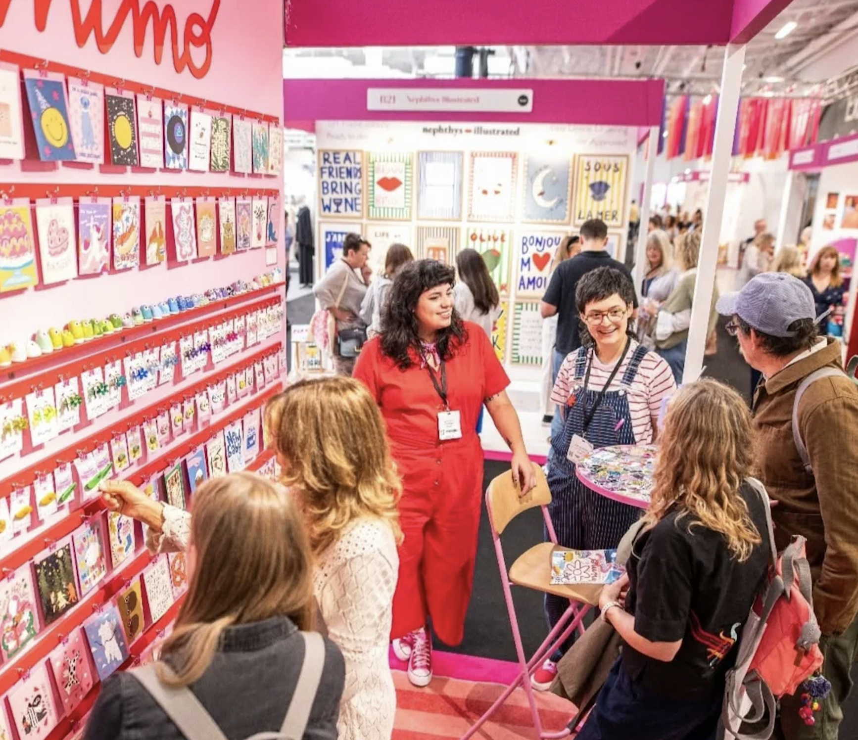 People browsing and shopping at a colorful greeting card and stationery booth at a fair or convention.