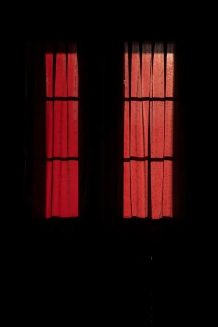 Two windows with red curtains, backlit, casting a red glow.
