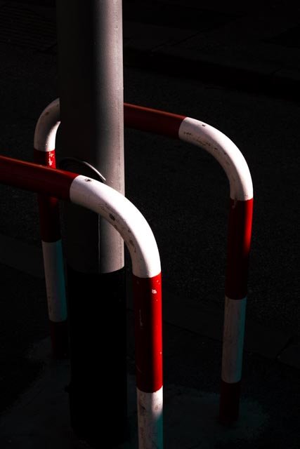 Red and white metal safety barriers around a grey metal pole in a dark area.
