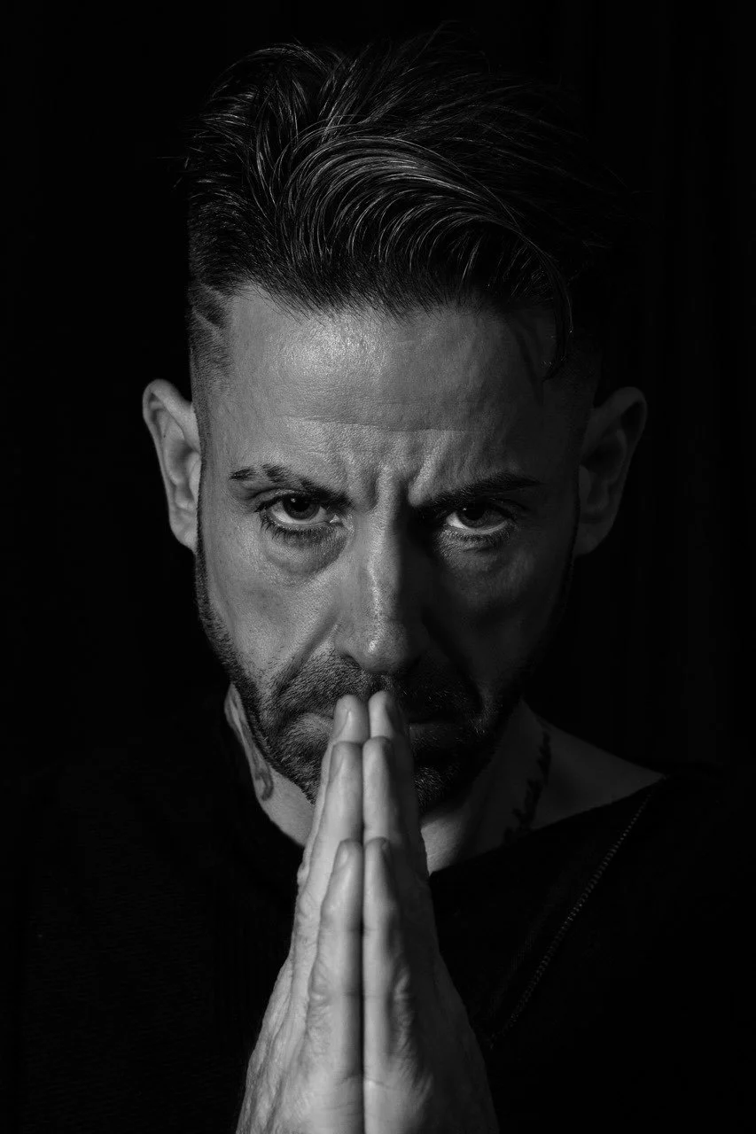 Portrait en noir et blanc d'un homme avec une expression intense, mains jointes près du visage et regard fixe.