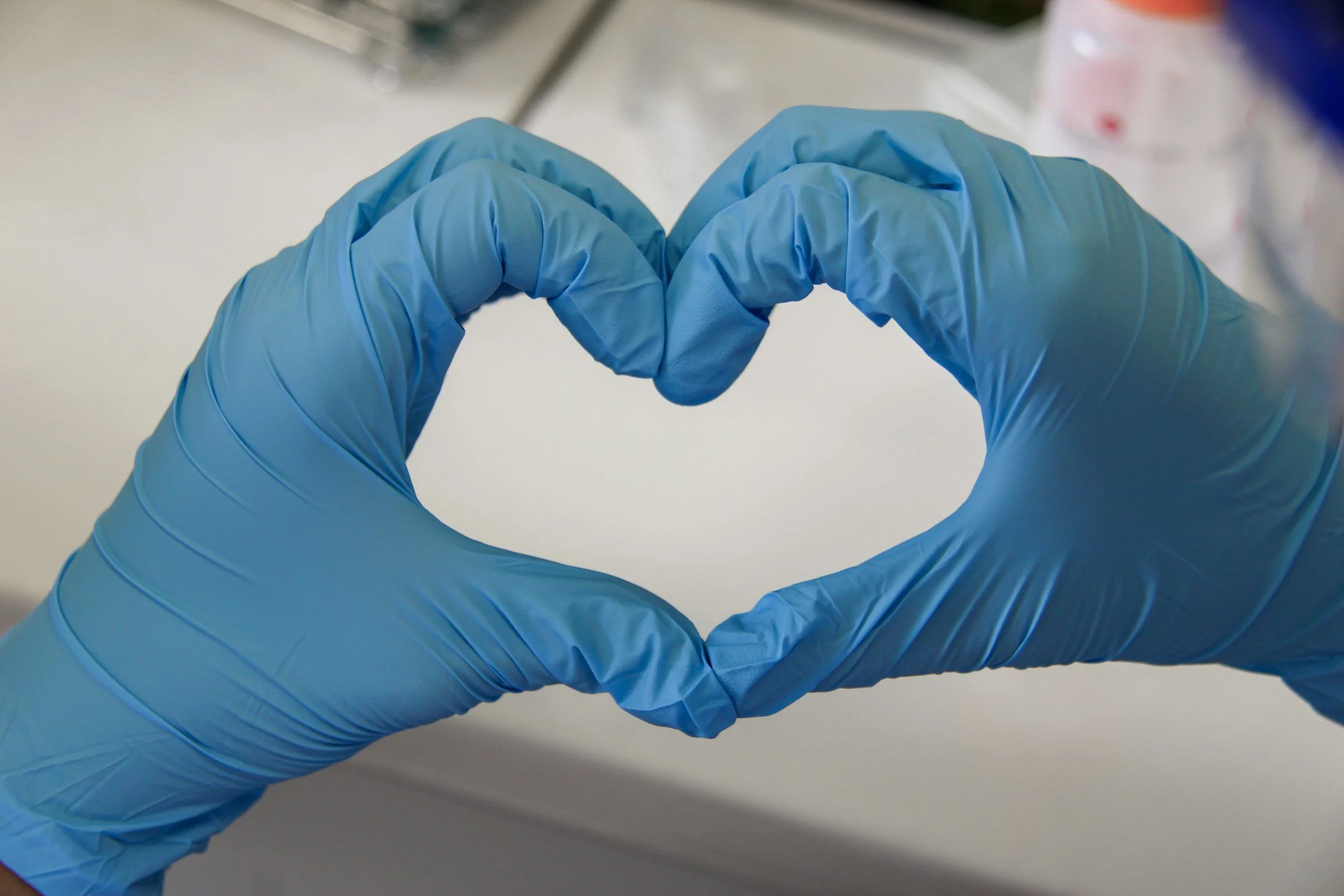 Hands wearing blue medical gloves forming a heart shape.