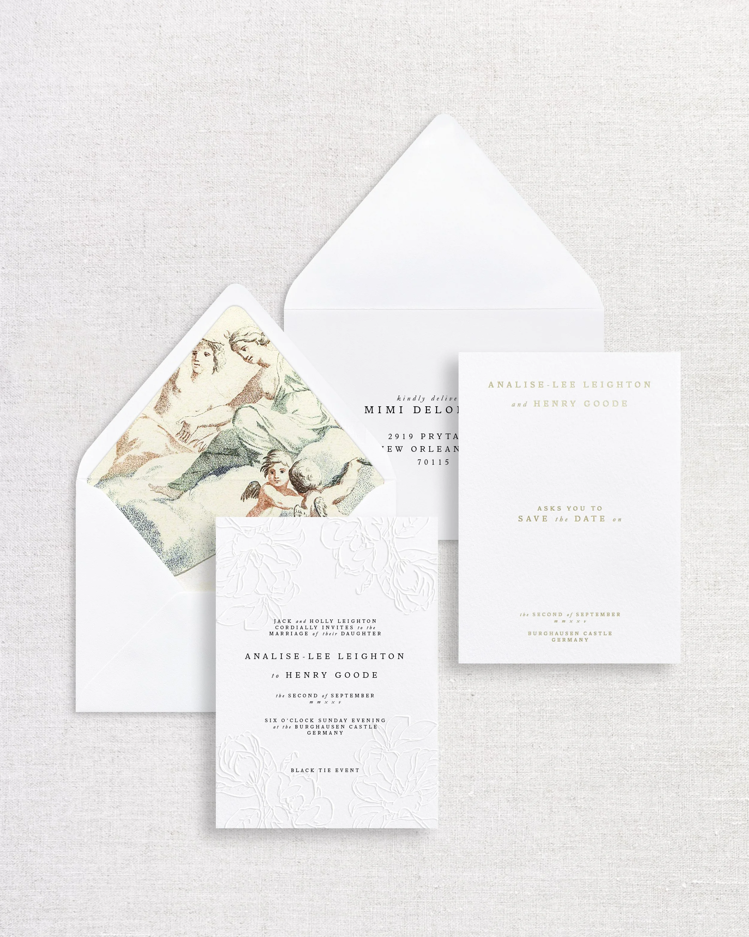 Wedding invitation suite including an invite card, save-the-date card, and envelope with a vintage illustration on the inside flap, all set on a light-colored fabric background.