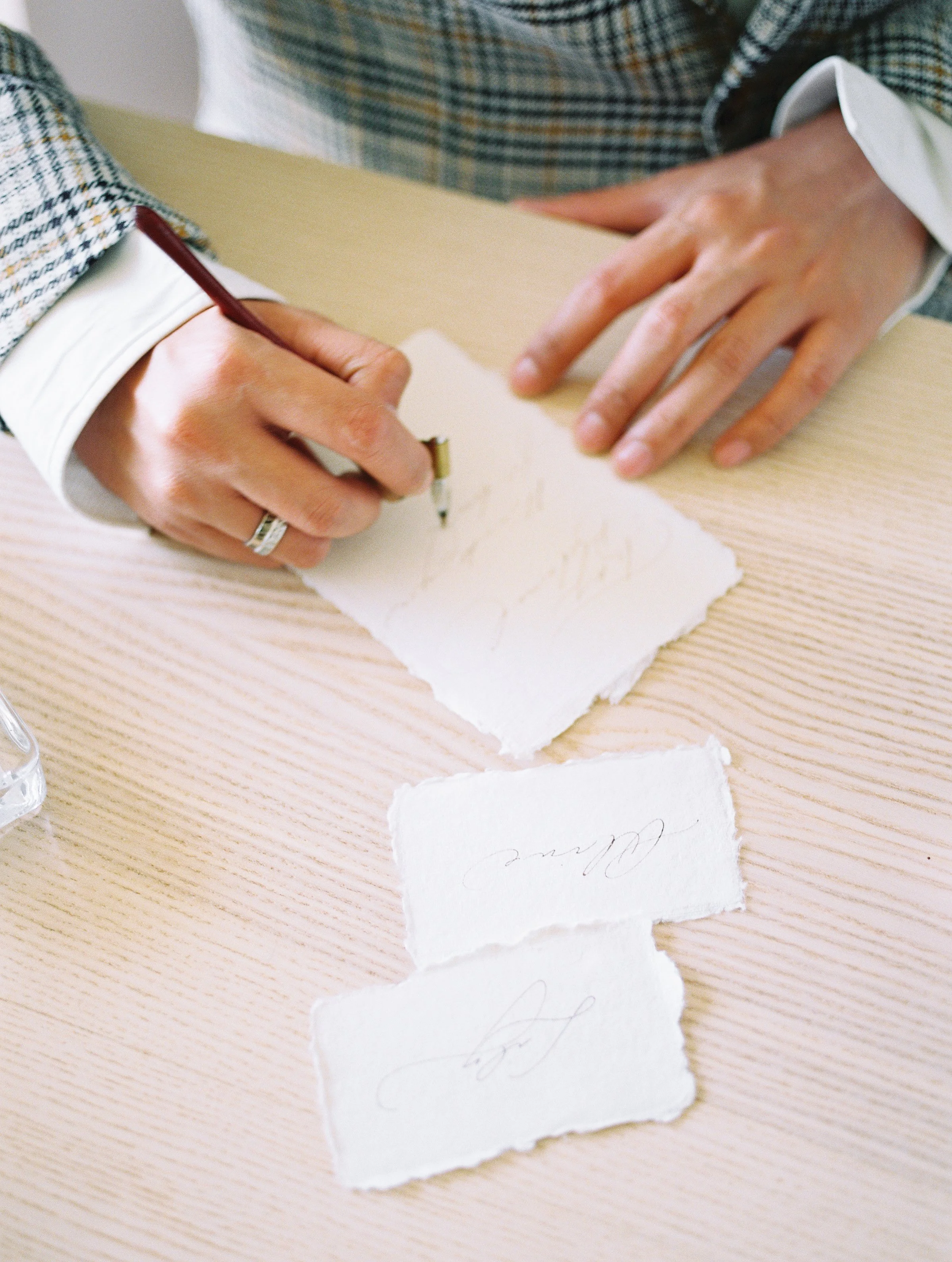 Person writing on torn paper with calligraphy pen on a wooden table.