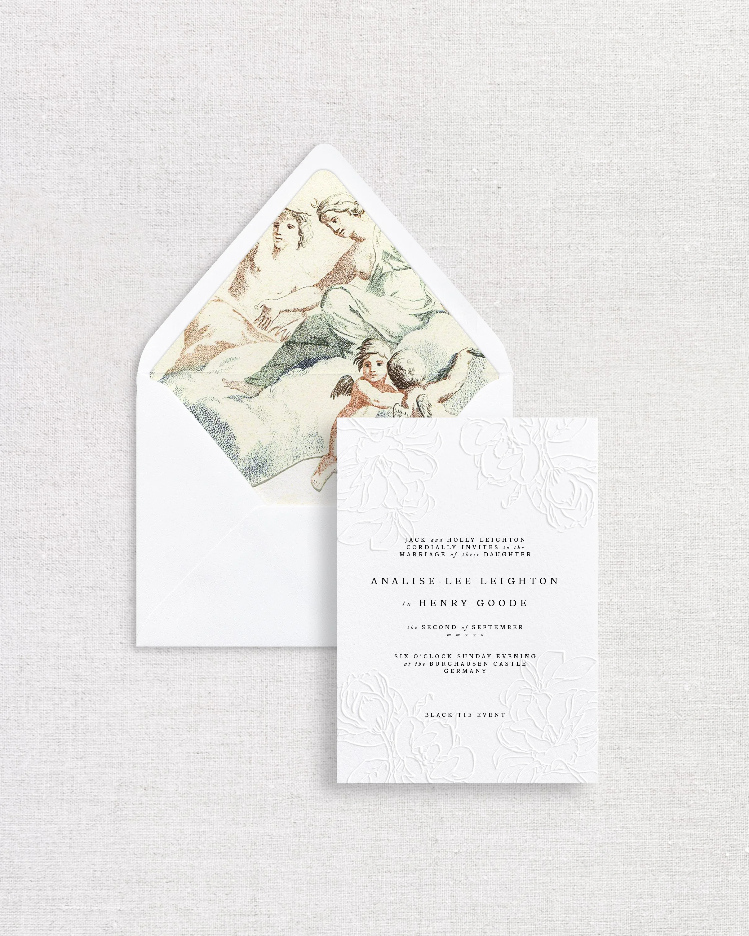 Wedding invitation card and envelope with a vintage style illustration inside, laid on a light fabric background.
