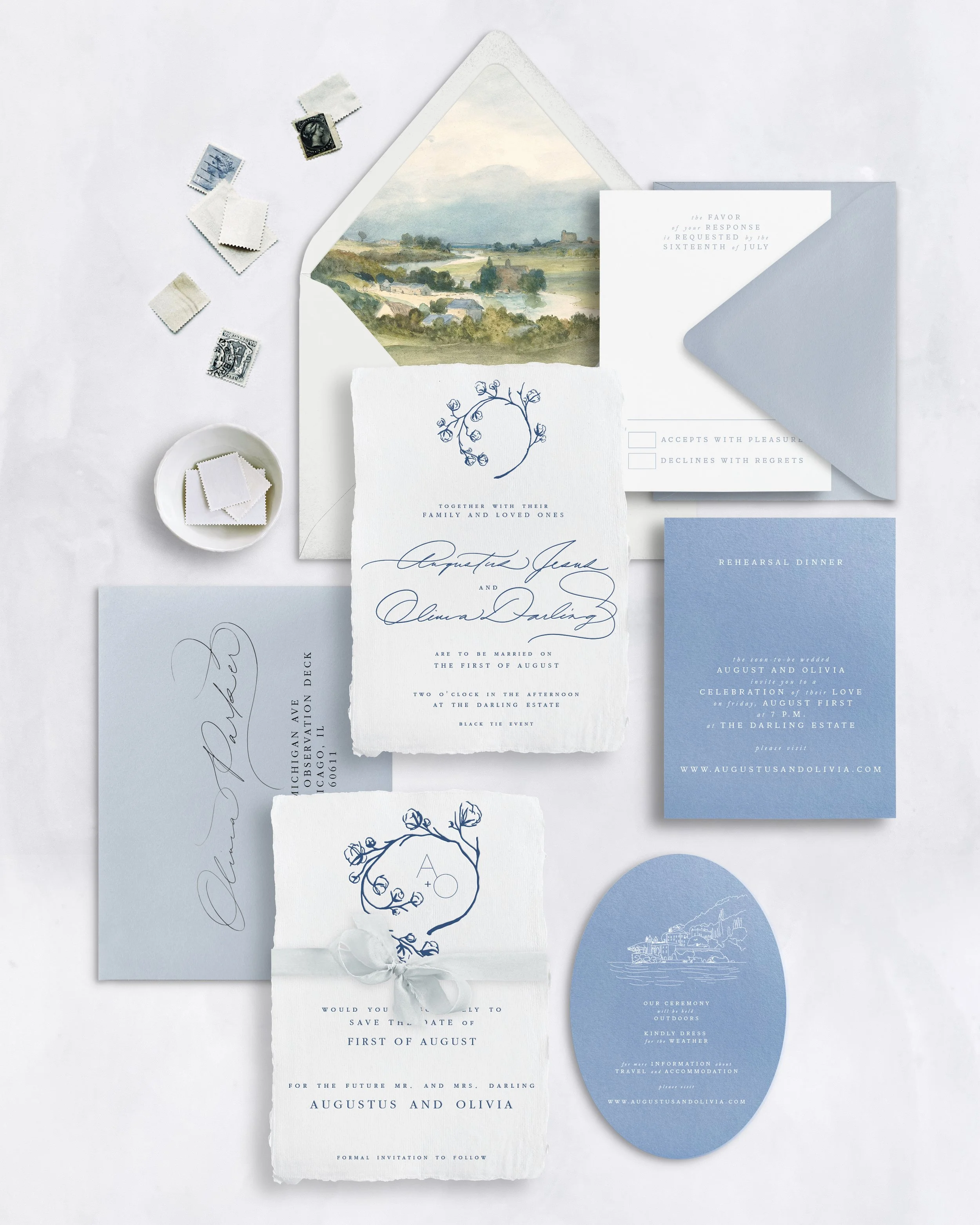 Wedding invitations and stationery in blue and white, with stamps and a small bowl of tags, arranged on a white surface.