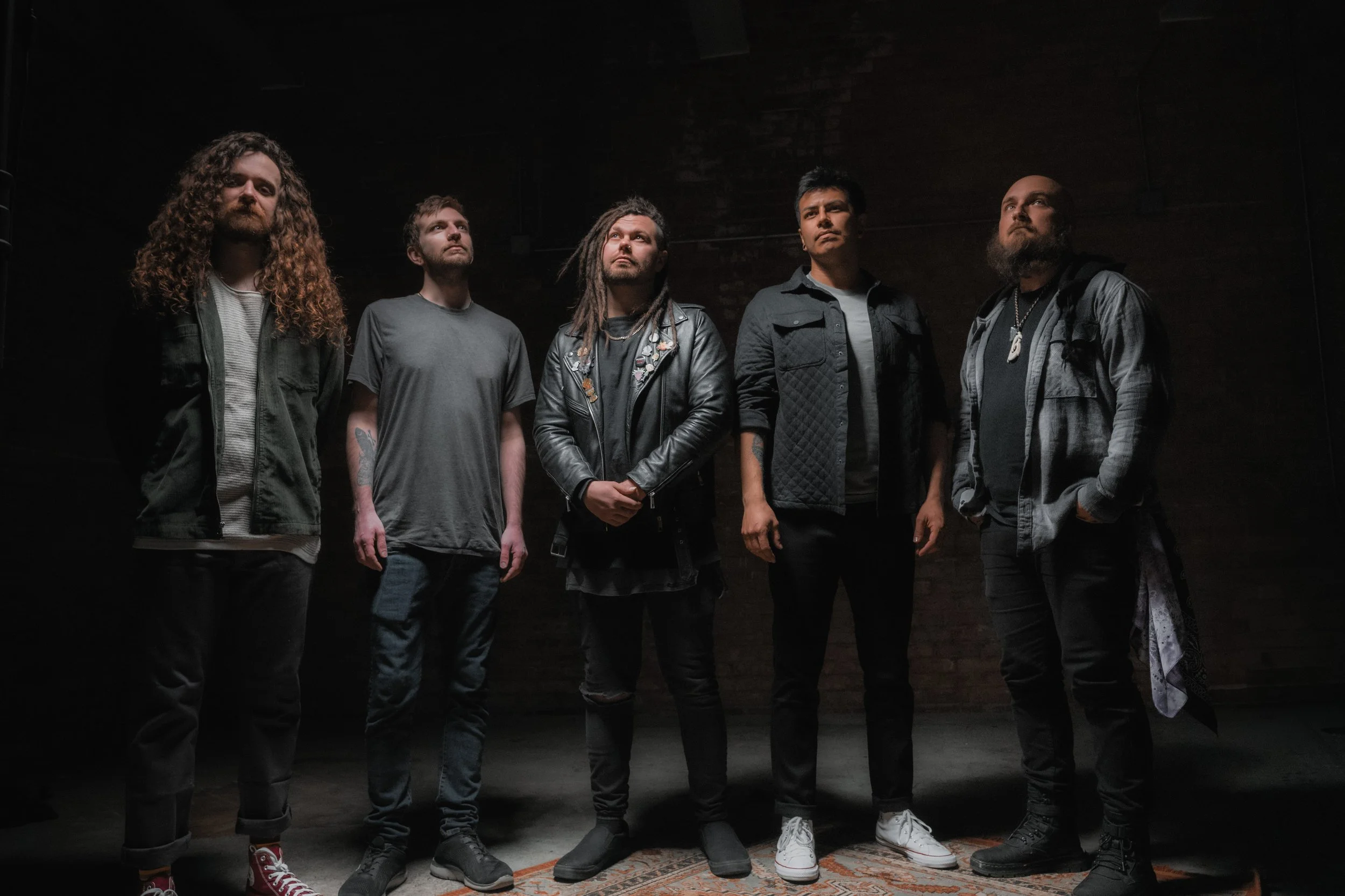 Five men standing in a dark room with a brick wall background, facing slightly upward. Sora Kai from Chicago, IL.