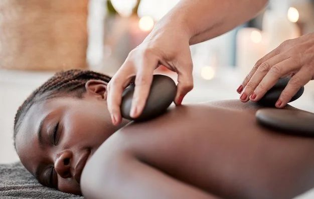 A woman receiving a hot stone massage on her back from a massage therapist.