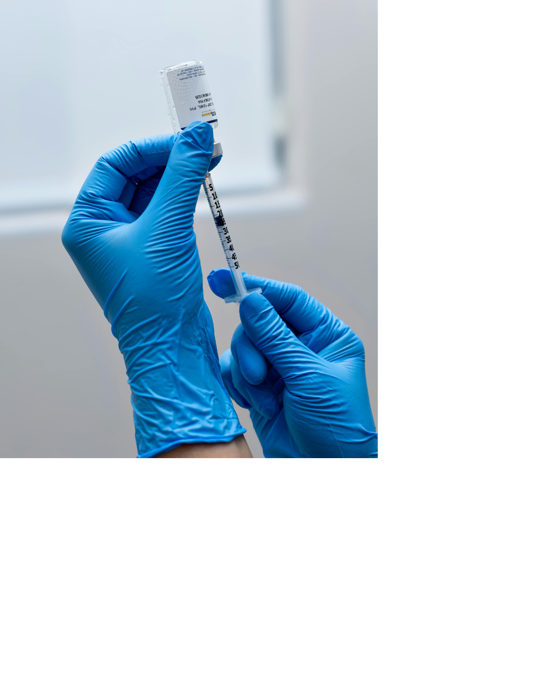 A person wearing blue gloves holding a syringe and a small vial, preparing for a medical injection.