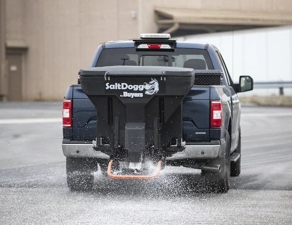 Action shot of a SaltDogg TGS07 salt spreader mounted to a Ford F150 spreading salt.