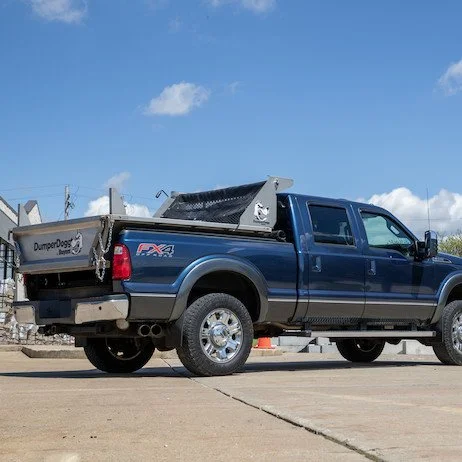 A blue pickup truck with a dump bed and ladder rack parked on a driveway under a blue sky with some clouds.