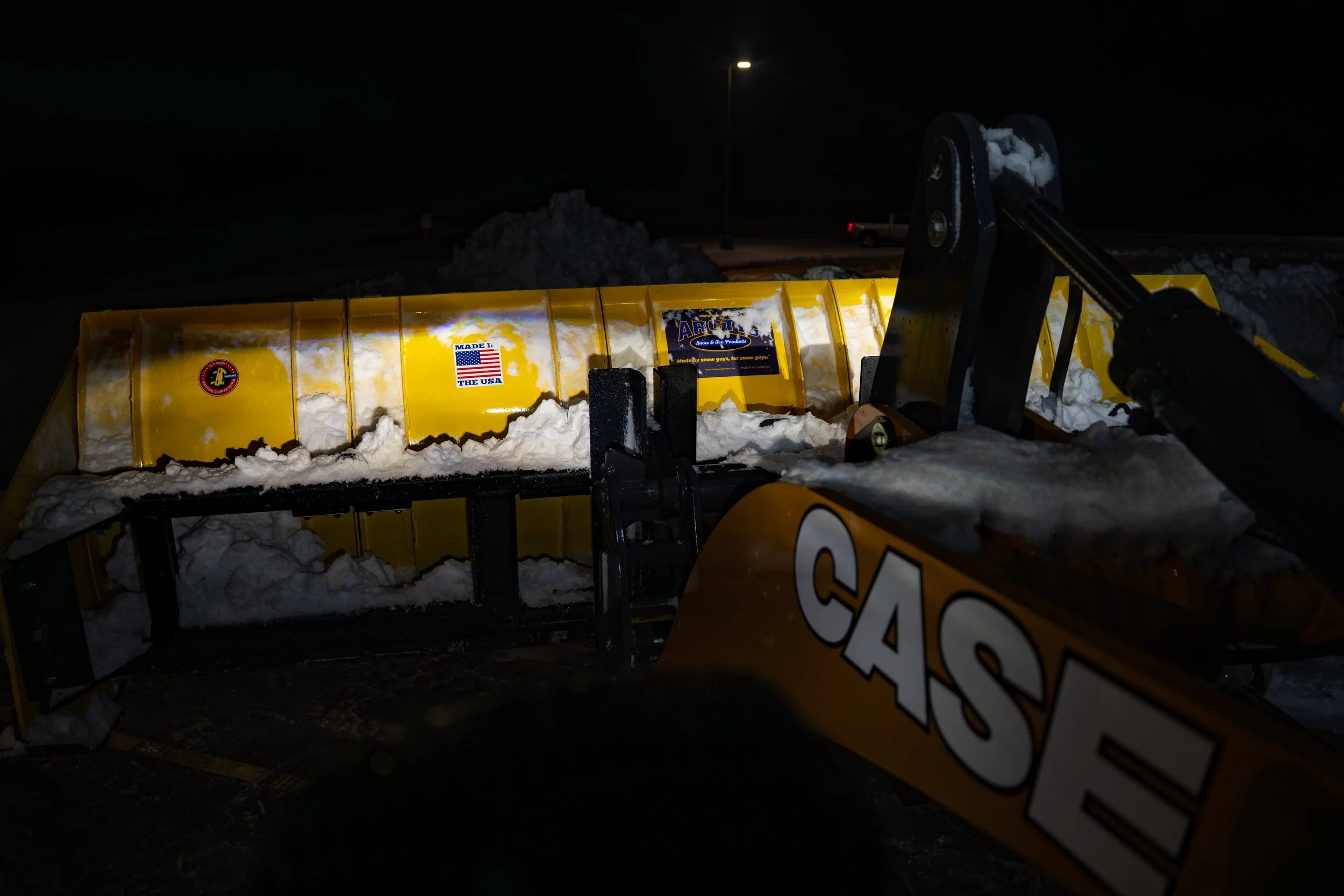 Sectional Arctic push box clearing snow at night, attached to a Case skid steer.