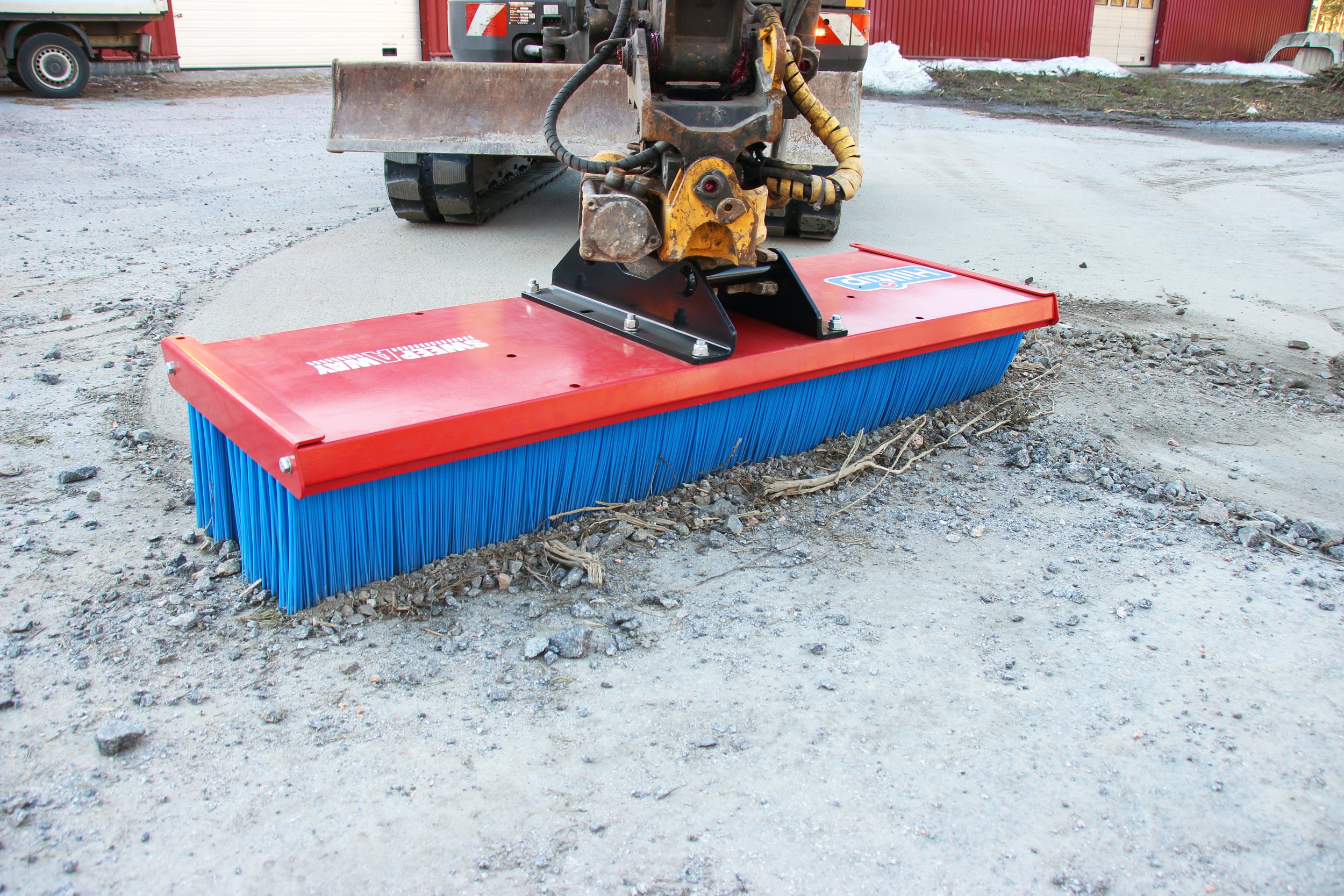 A ride-on power broom sweeping gravel and dirt on a construction site.