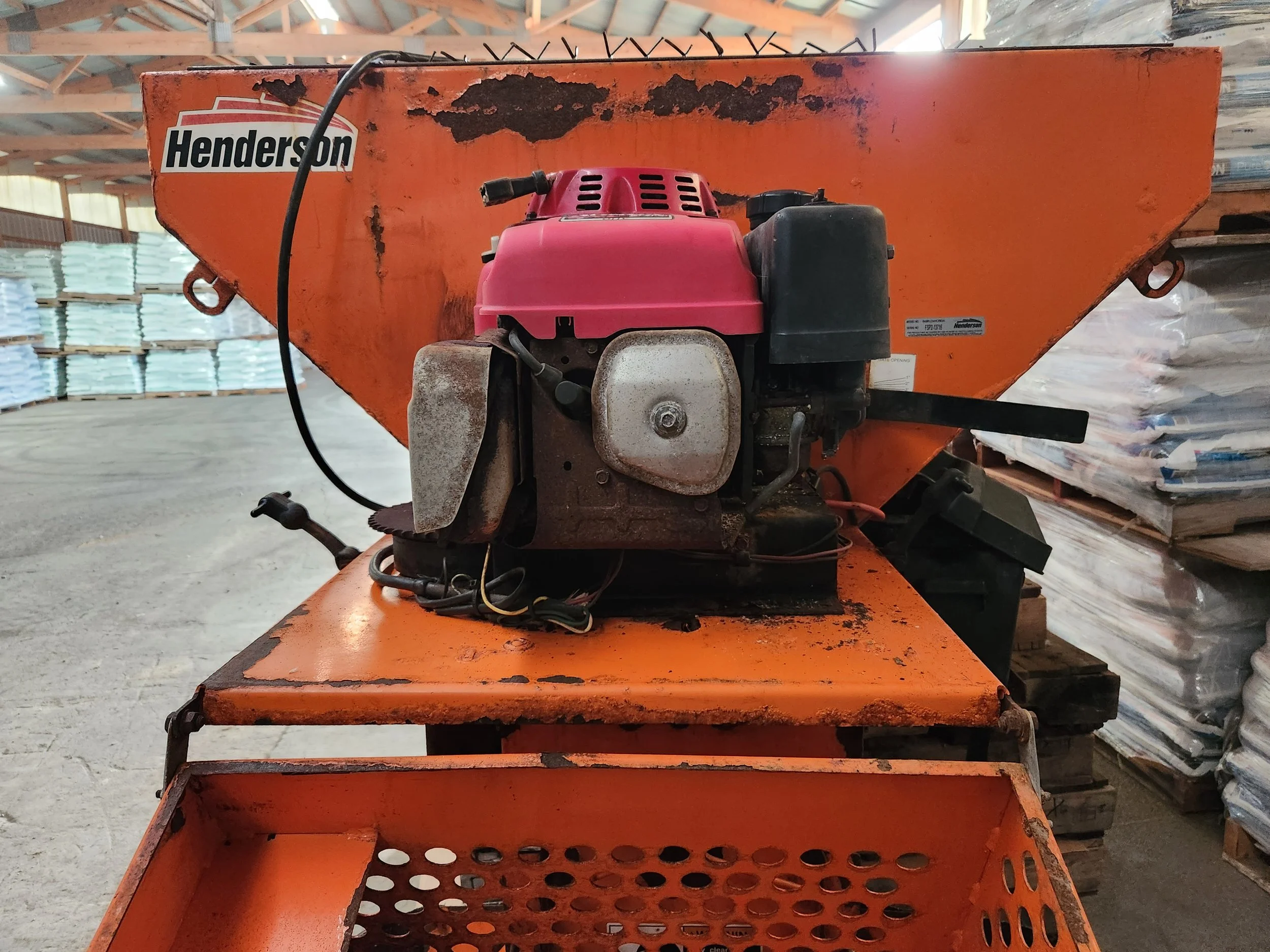 An orange industrial machine with a black and pink engine inside a warehouse. The machine is labeled Henderson and appears used with rust and dirt.