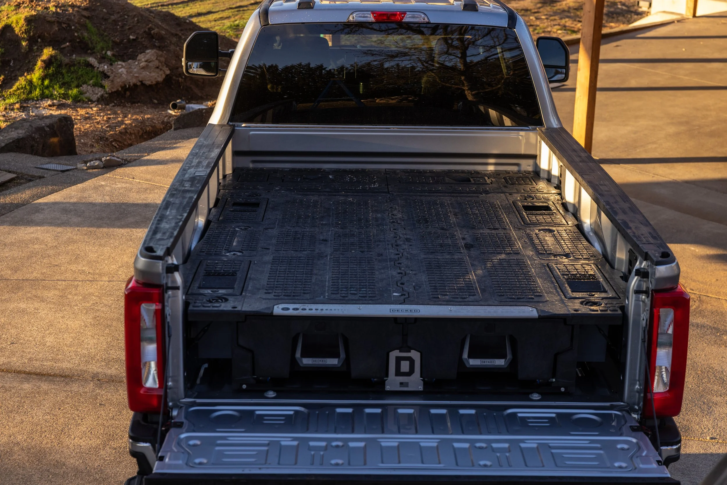 The back of a Ford pickup truck with a DECKED Drawer system installed, parked on a concrete driveway during sunset.