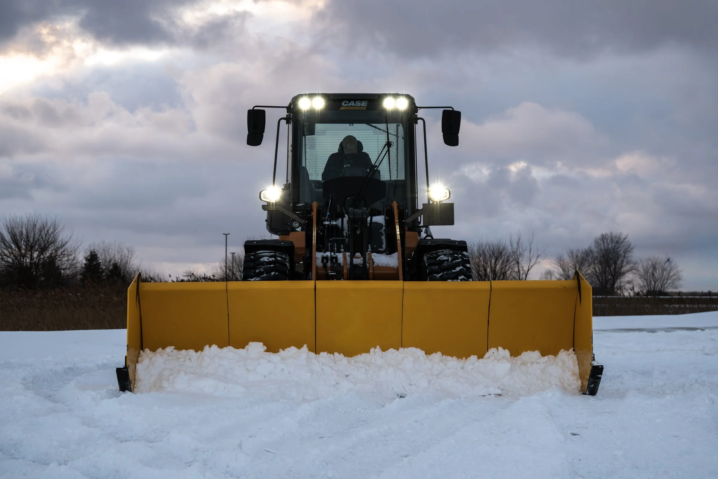 A sectional ARCTIC push box clearing snow from a road during cloudy weather in daytime.