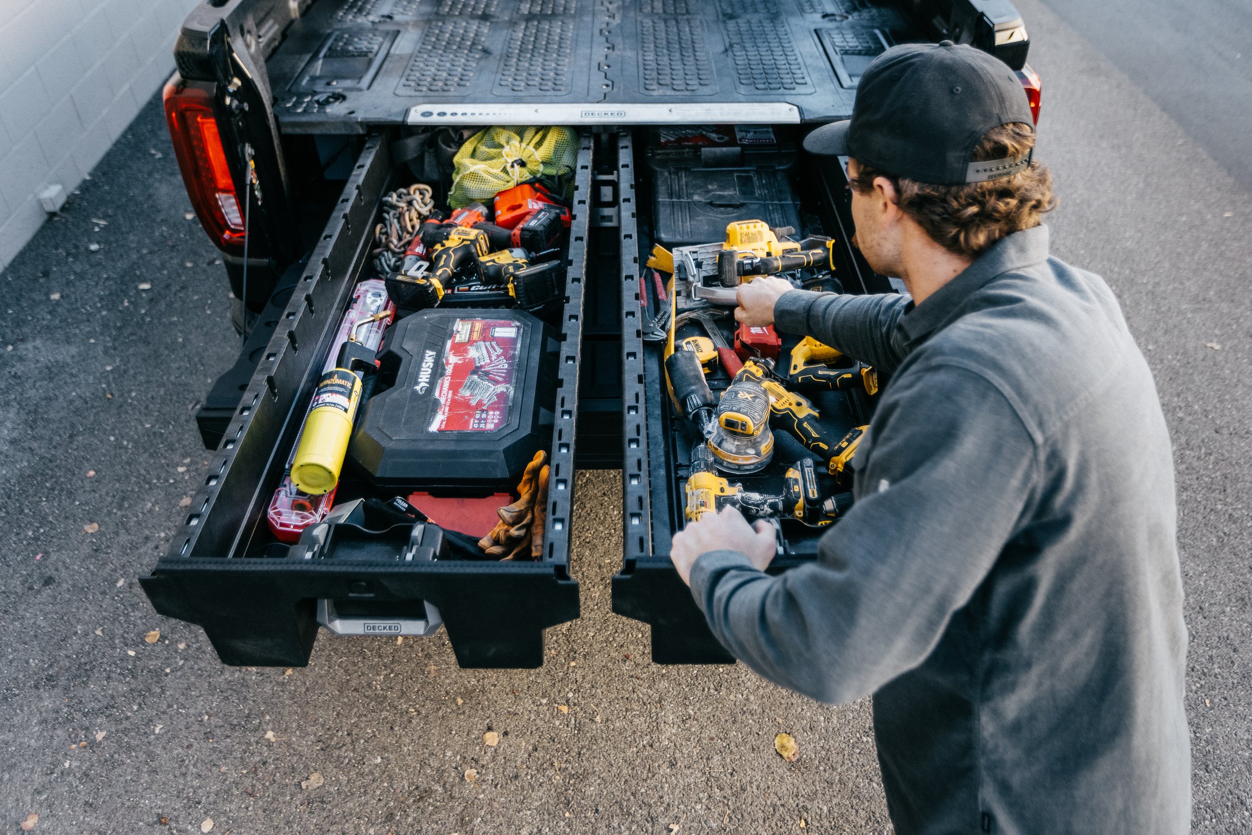 Man organizing tools in a DECKED equipped truck bed with a variety of power tools, toolboxes, and equipment.